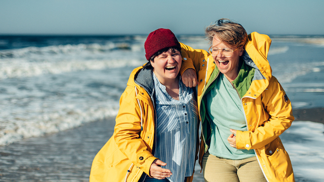 Zwei Frauen in gelben Jacken stehen am Meer.
