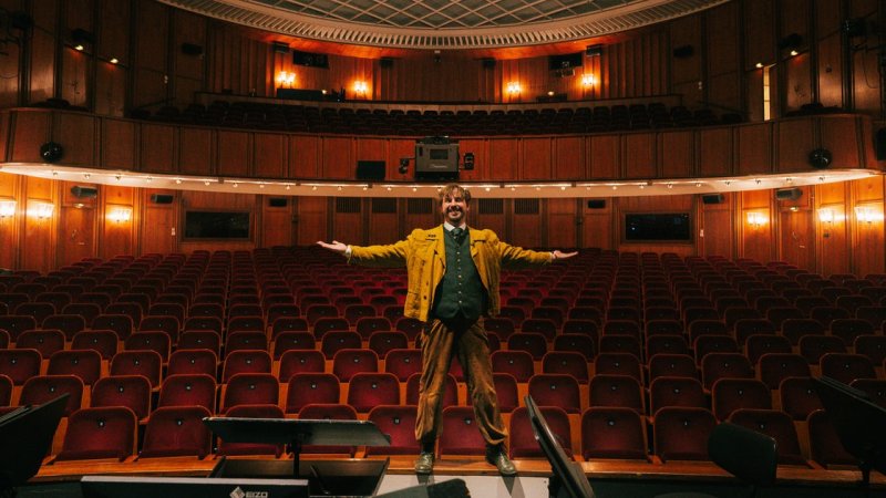 Phil Porter steht auf der Bühne, hinter ihm der leere Theatersaal