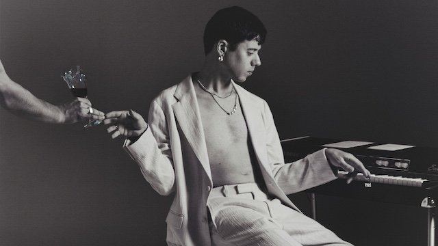 Der Sänger von Dressed Like Boys sitzt an einem alten Keyboard und bekommt ein Glas Wein gereicht. Das Bild ist in Schwarz-Weiß